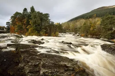a river with rapids on top of rocks and trees at Garth Cottage - Riverside with Private Hot Tub in Killin