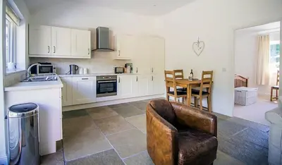 a kitchen with white cabinets and a chair and a table at Garth Cottage - Riverside with Private Hot Tub in Killin