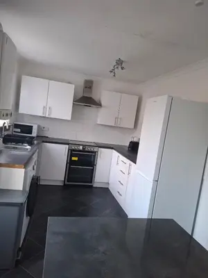 a kitchen with white cabinets and a black floor at Cheerful 3 bedroom house with free parking in Hurlet