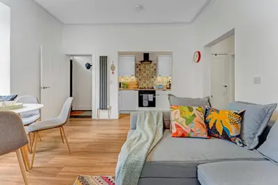 a living room with a gray couch and a kitchen at Stylish 2-Bed Villa Garden Central Edinburgh in Edinburgh