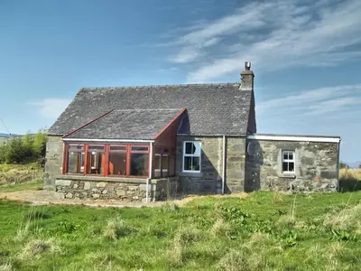 a small stone house in a field with grass at Finchairn Cottage in Lochgilphead