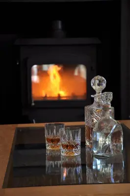 a bottle of whiskey and glasses on a table with a fireplace at Finchairn Farmhouse in Lochgilphead