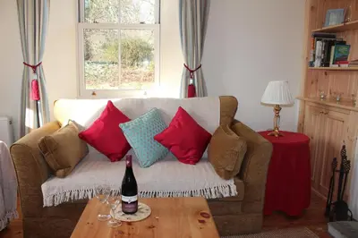 a couch with pillows and a bottle of wine on a table at The School House in Lochgilphead