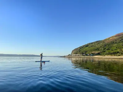 a person standing on a paddle board in the water at The Green in Lochranza