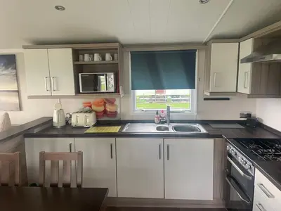 a kitchen with white cabinets and a sink and a window at Shells at Sandylands in Stevenston