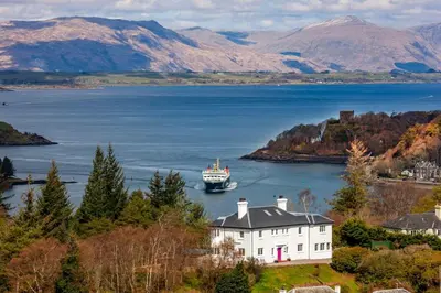 a boat in a large body of water with a house at Oban Bay Hall in Dunollie