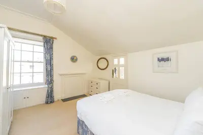 a white bedroom with a bed and a window at Top floor, central, spacious, period apartment with park views in Edinburgh