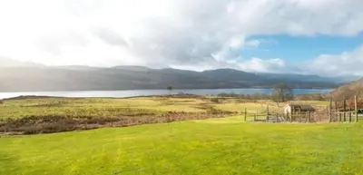 a field of green grass with a lake in the background at Coach House at Morenish Mews in Killin