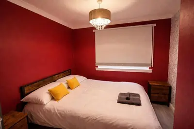 a red bedroom with a bed with yellow pillows and a window at Comfortable 3 Bed Home with Garden & Parking Stylish Family Contractor in Newton Mearns