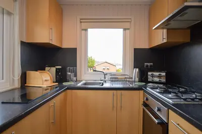 a kitchen with wooden cabinets and a sink and a window at Heather Lodge with Hot Tub in Hunters Quay