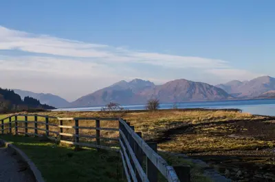 a fence next to a body of water with mountains at The Ballachulish Hotel in Glencoe
