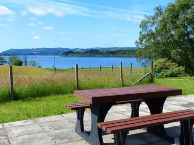 a wooden picnic table with a view of a lake at Blarghour Farm Cottages Overlooking Loch Awe in Ardchonnell
