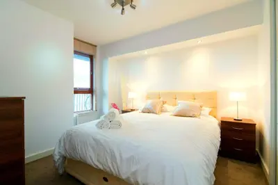 a bedroom with a bed with white sheets and a window at Mitchell Street Glasgow Apartment in Glasgow