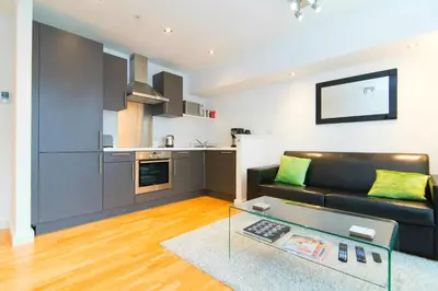 a living room with a black couch and a kitchen at Mitchell Street Glasgow Apartment in Glasgow