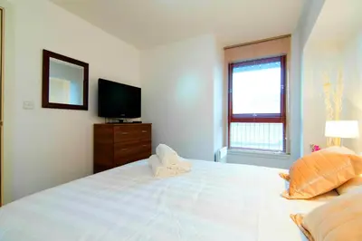a bedroom with a large white bed and a television at Mitchell Street Glasgow Apartment in Glasgow