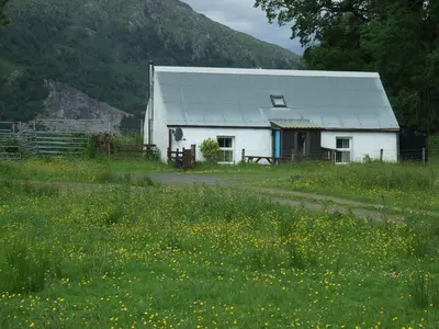 a white barn in a field of flowers at Inverawe Cottages in Taynuilt