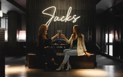 two women sitting on a bench in front of a neon sign at Dakota Glasgow in Glasgow