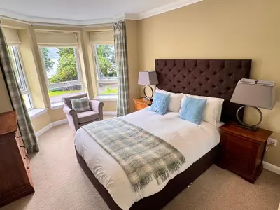 a bedroom with a bed and a chair and windows at Allt Nan Ros Apartments fort william in Onich