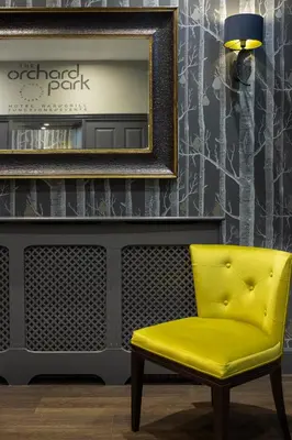 a yellow chair in front of a wall with a mirror at The Orchard Park Hotel in Giffnock