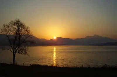 a sunset over a body of water with a tree at Tigh Grianach in Connel