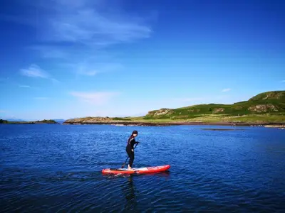 a man is standing on a paddle board in the water at Tigh Beg Croft in Lerags