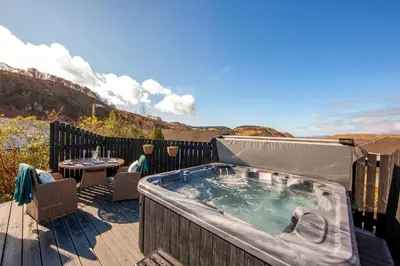 a hot tub on a deck with a table and a patio at Katie's Flat in Oban