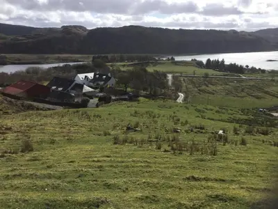 a field of grass with a house and a river at Oban Seil Farm in Clachan