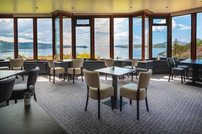 a restaurant with tables and chairs and large windows at Loch Melfort Hotel in Ardfern