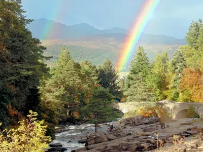a rainbow over a river with trees and a mountain at Gracedieu in Killin