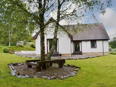 a bench in front of a house with a tree at Bethany Cottage in Aberfoyle