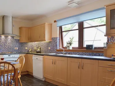 a kitchen with wooden cabinets and a large window at Bethany Cottage in Aberfoyle