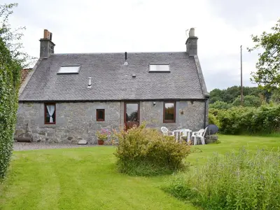 an old stone house with a table and chairs in a yard at Ross Cottage in Cairneyhill