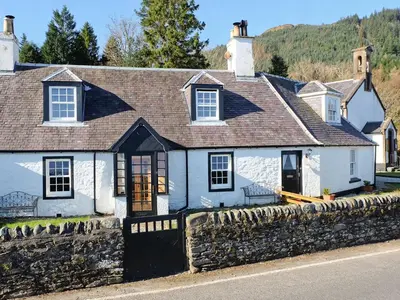 a white house with a stone wall at Fern Cottage in Ardentinny