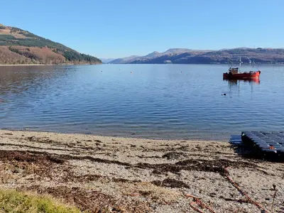 a red boat in the water next to a beach at Fern Cottage in Ardentinny