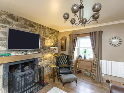 a living room with a fireplace and a tv on a stone wall at Fern Cottage in Ardentinny