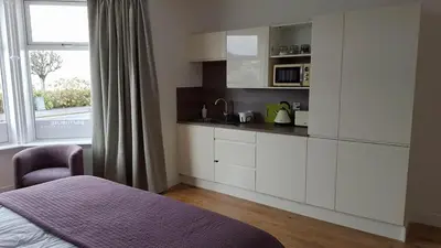 a bedroom with a kitchen with white cabinets and a window at Boat House Super Suites in Rothesay