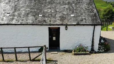 a white building with a black door and a roof at Garrison Farm with Hot Tub in Inversnaid