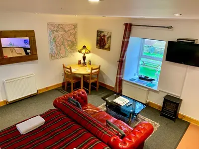 a living room with a red leather couch and a table at Garrison Farm with Hot Tub in Inversnaid