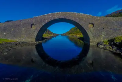 an old stone bridge with a reflection in the water at Tramway Cottages in Ellanbeich