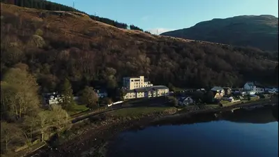 a building on a hill next to a body of water at Loch Long Hotel in Arrochar