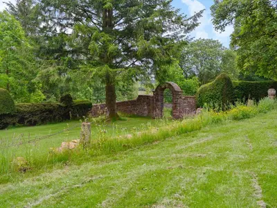 an old stone building with a tree in a field at Gilminscroft Gatehouse in Sorn