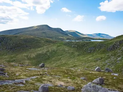 a green hillside with rocks and mountains in the background at Culsharg Cottage in Bargrennan