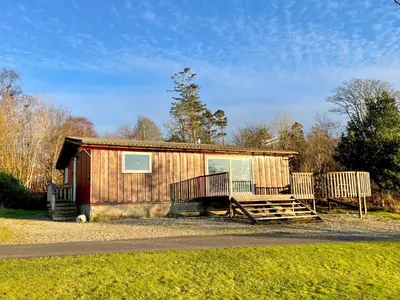 a small wooden cabin with a porch on a road at Cockleshell Lodge in Otter Ferry