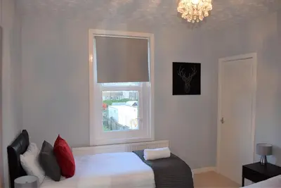 a bedroom with a bed with a window and a chandelier at Kelpies Serviced Apartments - Wallace in Falkirk