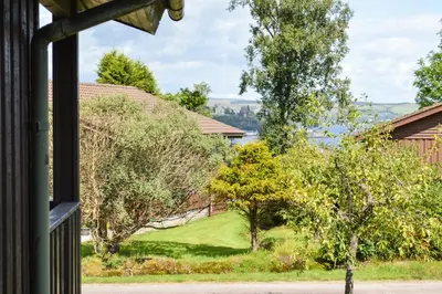 a view from a house window of a yard with trees at Holy Loch Lodge in Hunters Quay