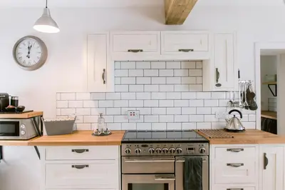 a kitchen with white cabinets and a clock on the wall at Dunruadh Cottage in Gartocharn