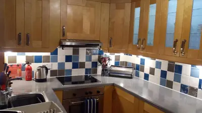 a kitchen with wooden cabinets and blue and white tiles at Feochan View in Oban