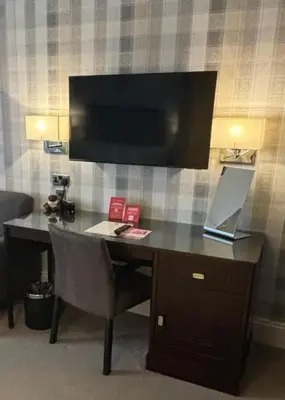 a desk with a laptop and a television on a wall at Leonardo Edinburgh City in Edinburgh
