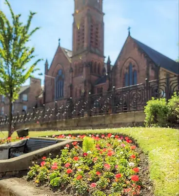 a church with a clock tower and flowers in front of it at Kelpies Serviced Apartments in Falkirk