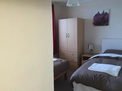 a bedroom with two beds and a cabinet and a table at Laughing Buddha Guesthouse in Uddingston
